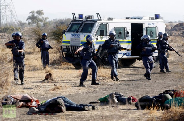 A policeman gestures in front of some of the dead miners after they were shot outside a South African mine in Rustenburg